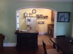 Kitchen features a central island with sink and bar stools, a refrigerator, and a clock above.
