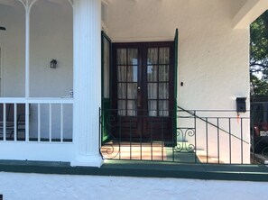 Traditional building with a classic entrance featuring a dark door, white columns, and a porch with a metal railing.