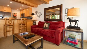 A cozy living room with a red sofa, wooden chairs, a coffee table, and a bookshelf. - RMR: La Choumine 8 Condo in Teton Village / Steps from the Mountain! (Teton Village)