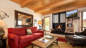 A cozy living room with a red sofa, a coffee table, and a fireplace. - RMR: La Choumine 8 Condo in Teton Village / Steps from the Mountain! (Teton Village)
