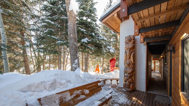 A wooden bench with snow on it, a wooden deck, and a building with a wooden exterior and a door. - RMR: La Choumine 8 Condo in Teton Village / Steps from the Mountain! (Teton Village)