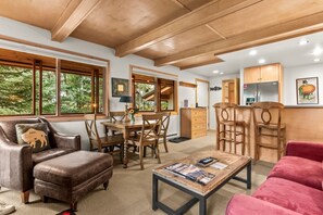 A spacious living area with a leather sofa, wooden dining table, and chairs, a red couch, and a kitchen area with wooden cabinets and a refrigerator. - RMR: La Choumine 8 Condo in Teton Village / Steps from the Mountain! (Teton Village)