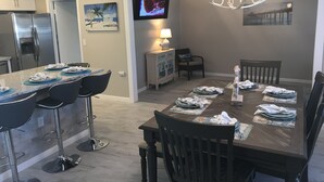A dining area with a wooden table set for four, bar stools, a television mounted on the wall, and a chandelier. -  Paradise Cove -- A perfect Beach Getaway (Bradenton)
