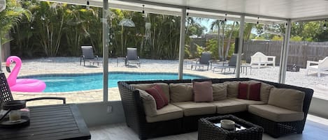 A covered patio with a pool, wicker furniture, and outdoor chairs.