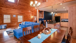 Ein geräumiges Wohnzimmer mit blauem Sofa, einem Holzespeisetisch und einer Küchenzeile mit Holzschränken und einem schwarzen Kühlschrank.