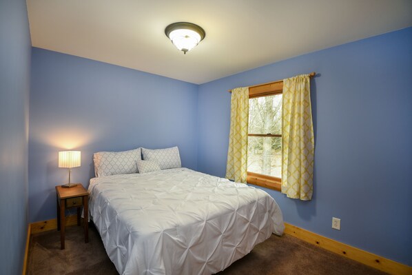 A bedroom with a bed, a nightstand, a lamp, and a window with curtains.