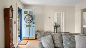 Un soggiorno con una porta blu, un divano floreale e una sveglia di legno.
