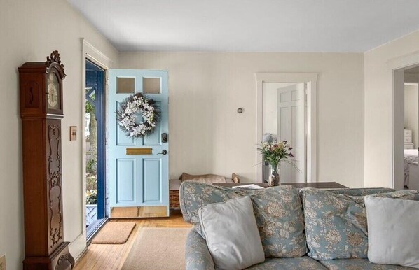 A living room with a blue door, a floral sofa, and a wooden clock.