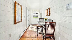 Un corridoio stretto con pareti bianche, una porta in legno, un tavolo da pranzo con sedie e una finestra con vista.