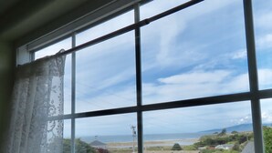 A view through a window with a lace curtain, revealing a coastal landscape with houses, a power line, and a distant mountain. - Enjoy Fresh Ocean Breezes, No Crowds In Small Community Setting (Bodega Bay)