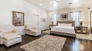 Une chambre à coucher avec un grand lit, deux fauteuils, un canapé, un ventilateur de plafond et une table de chevet avec une lampe.
