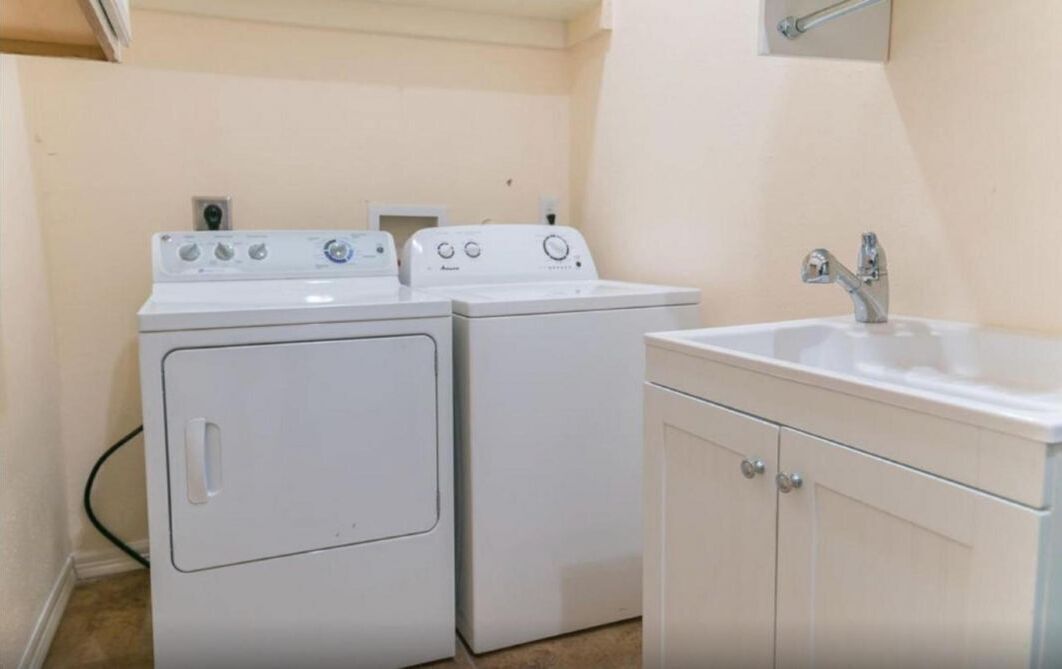 Un cuarto de lavandería con dos lavadoras blancas y un lavamanos.