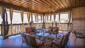 Un espace extérieur abrité, doté d’un plafond en bois, de chaises en métal, d’une table en verre et de rideaux.