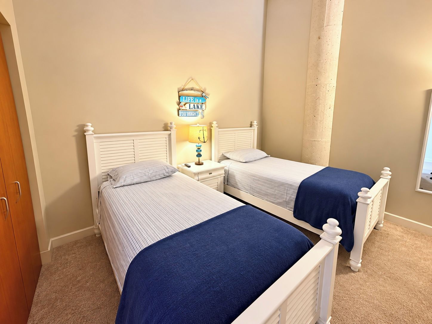 A bedroom with two single beds, a nightstand with a lamp, and a wall-mounted sign.