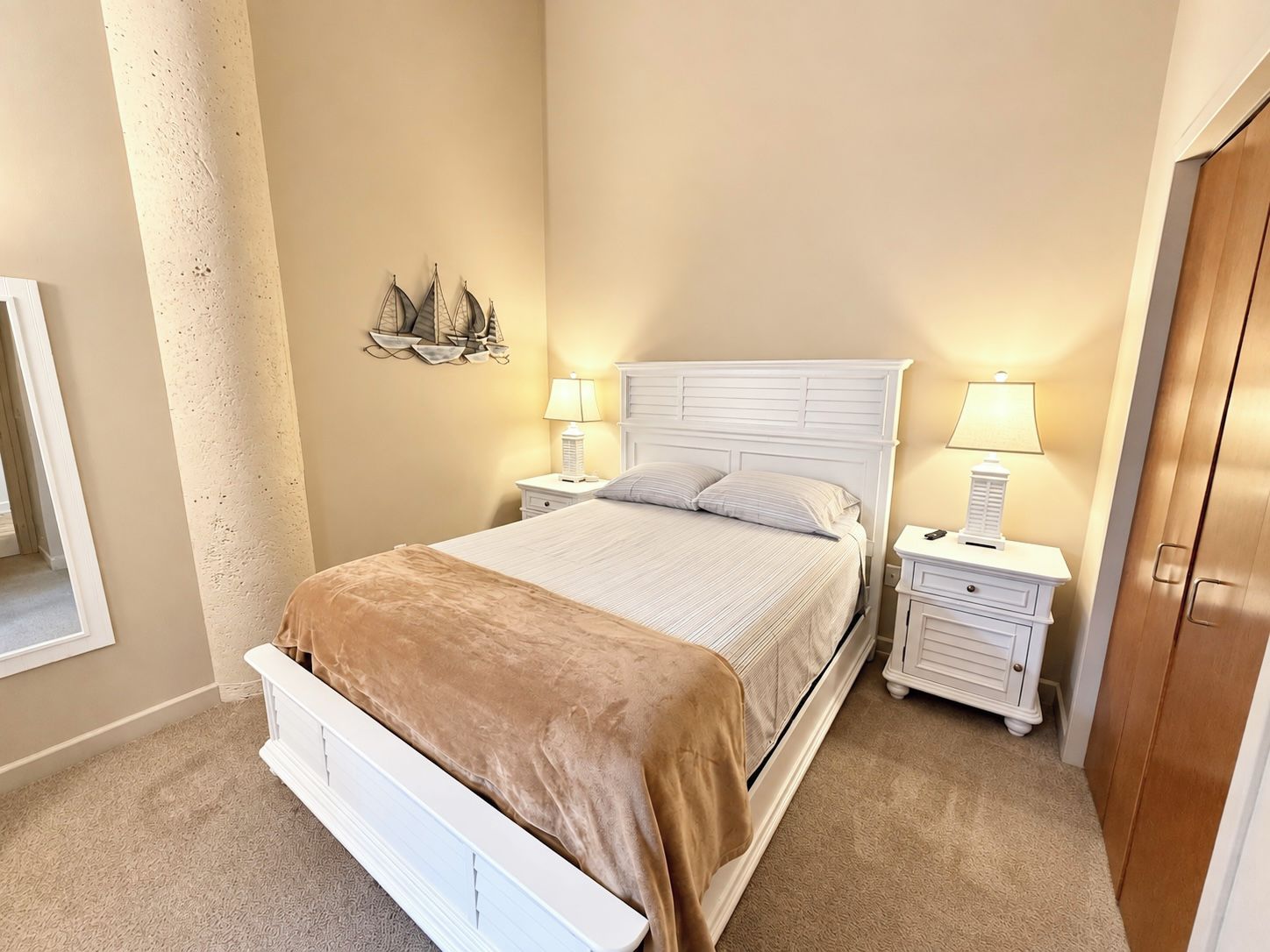 A bedroom with a bed, two bedside tables with lamps, a wall-mounted ship decoration, and a wooden door.