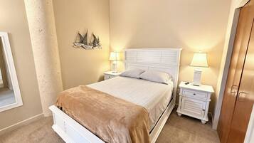 A bedroom with a bed, two bedside tables with lamps, a wall-mounted ship decoration, and a wooden door.