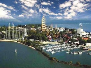 An aerial view of a coastal amusement park with roller coasters, a Ferris wheel, and a marina with boats.