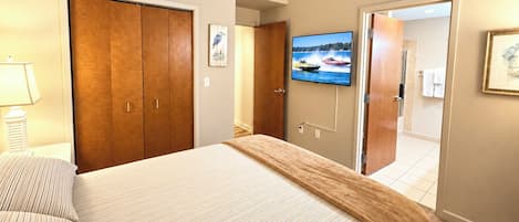 A hotel room with a bed, a TV mounted on the wall, a wooden wardrobe, and a bathroom visible through an open door.