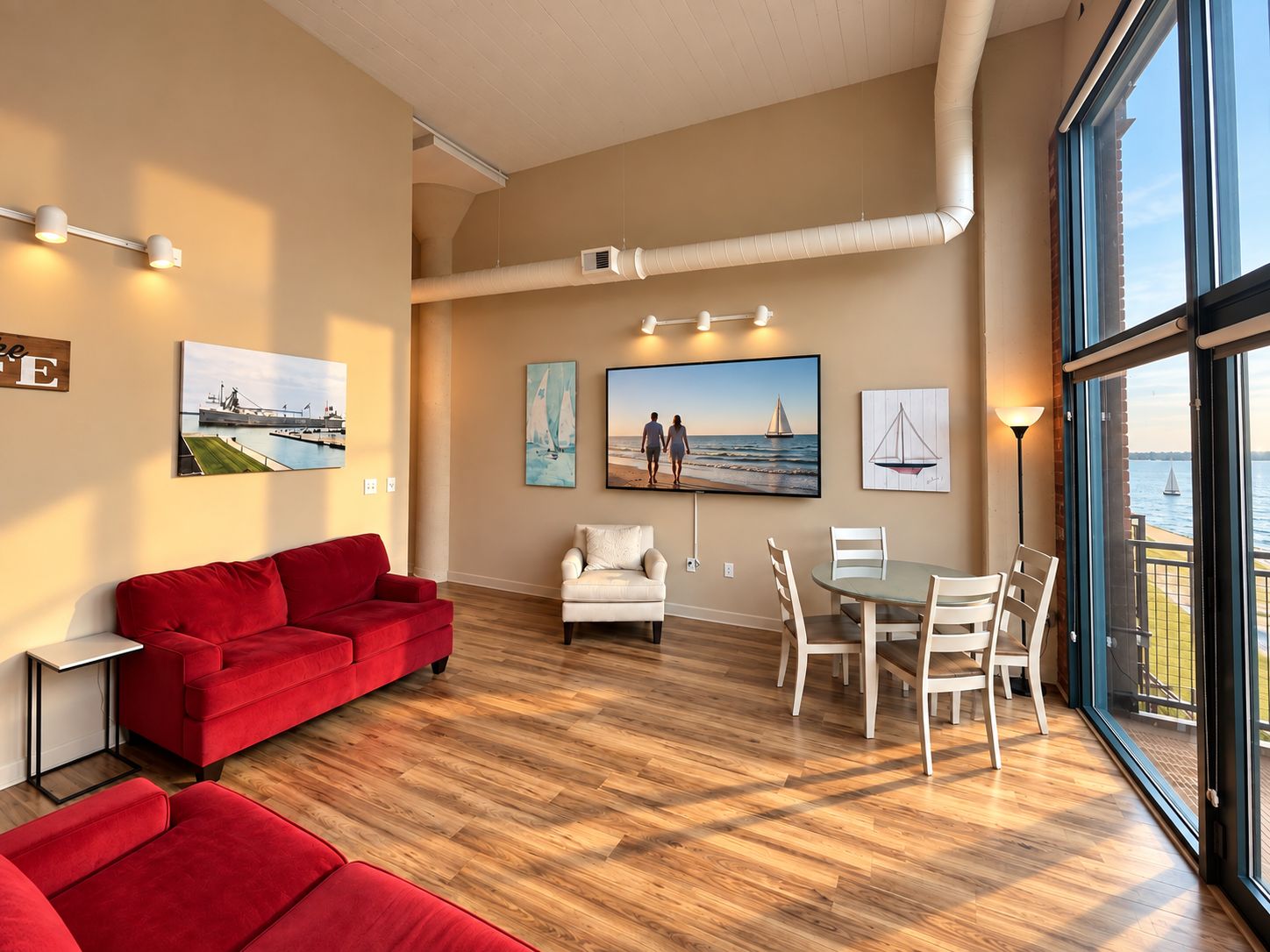 A spacious living area with a red sofa, a white armchair, a dining table with chairs, and large windows offering a view of the sea.