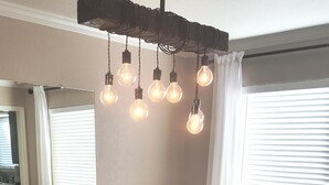 Een eetruimte met een donker houten tafel, vier gestoffeerde stoelen en een lamp met zichtbare lampen.