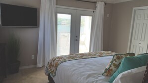 Een slaapkamer met een bed, een aan de muur bevestigde televisie en een deur die leidt naar een buitenruimte.
