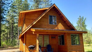 Puinen mökki, jossa on katettu kuisti, grilli ja sininen Adirondack-tyylinen puutarhatuoli.