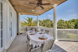 A covered outdoor dining area with a table set for four, surrounded by white railings and palm trees in the background.