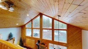 L’intérieur d’une cabane en bois, avec une grande fenêtre, un escalier et un luminaire suspendu.