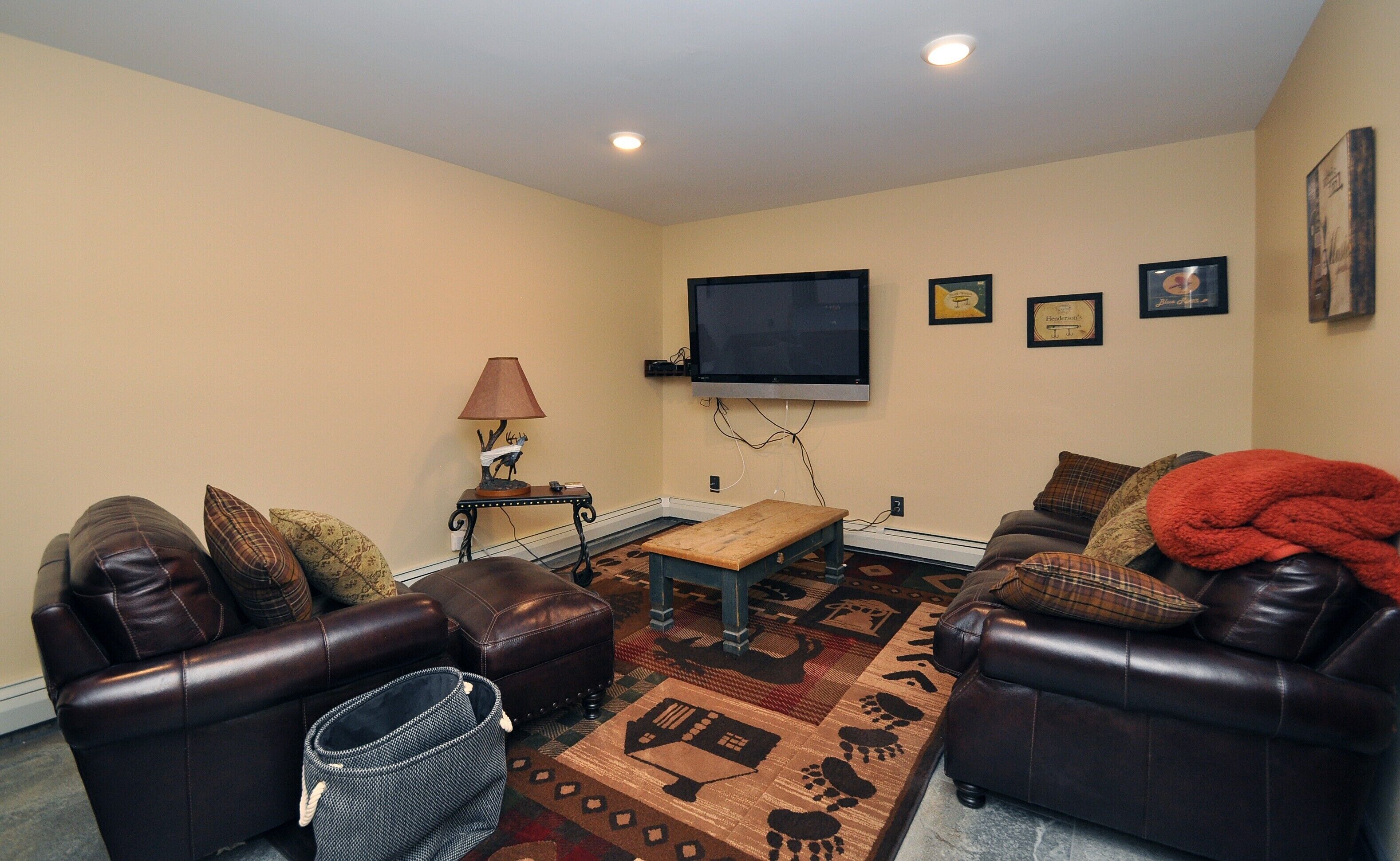 A living room with two leather sofas, a coffee table, a TV mounted on the wall, and a patterned rug.