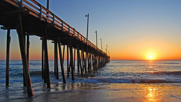 A pier extending into the water with a sunset in the background. - Hatteras Island Charmer! (Salvo)
