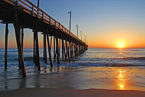 Un muelle que se adentra en el agua con un atardecer al fondo.