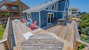 A wooden deck with a table and chairs, a small blue building with a door, and a wooden staircase. - Hatteras Island Charmer! (Salvo)
