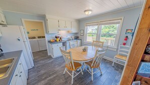 A kitchen with white cabinets, a wooden dining table with four chairs, a microwave, and a refrigerator. - Hatteras Island Charmer! (Salvo)