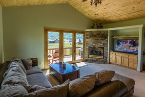 Uma sala de estar aconchegante com lareira de pedra, televisão e uma grande janela com vista para um deck.
