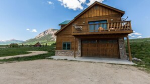 A two-story wooden house with a balcony, a stone foundation, and a garage. - Family Friendly - On Ten Acres 3 Miles to Town - Stunning Views and Country Feel (Crested Butte)