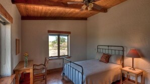 Um quarto com cama, escrivaninha, cadeira, janela e ventilador de teto.