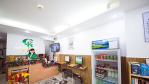 Un espace d’accueil doté d’un comptoir en briques, de deux écrans d’ordinateur, d’un téléviseur et d’un réfrigérateur rempli de boissons.