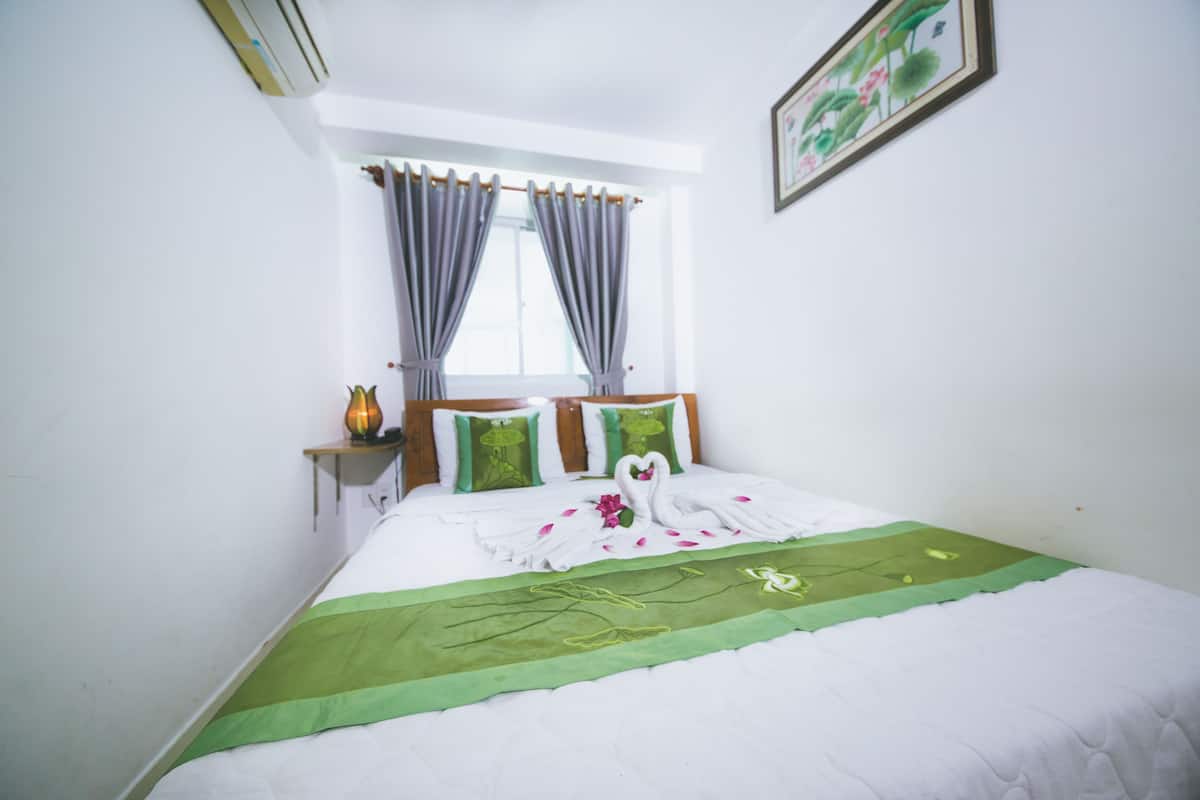 Cama bem arrumada com colcha verde, almofadas brancas e arranjo decorativo de toalhas em formato de cisne.