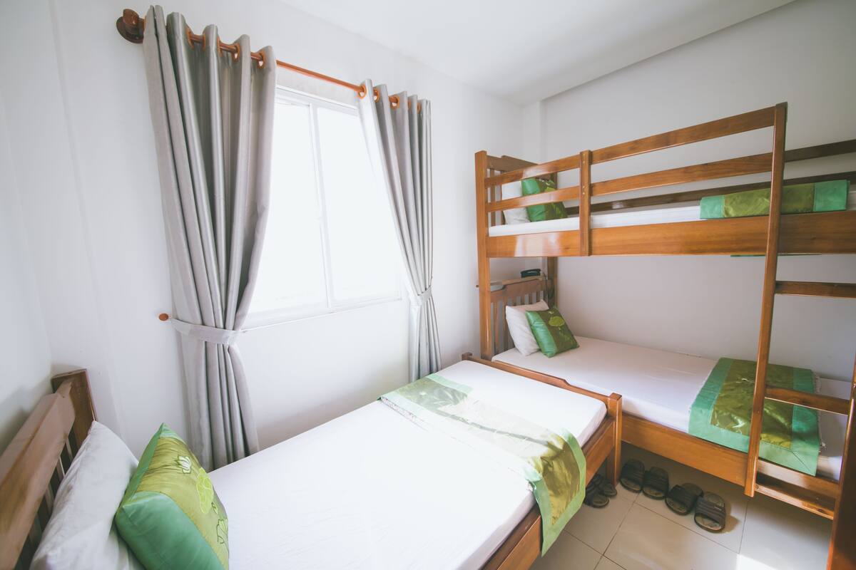 Quarto com duas camas de solteiro, uma janela com cortinas e uma beliche.