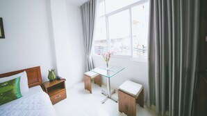 Une chambre d’hôtel avec un lit, une petite table sur laquelle est posé un vase de fleurs, une table de chevet en bois et une fenêtre avec des rideaux.