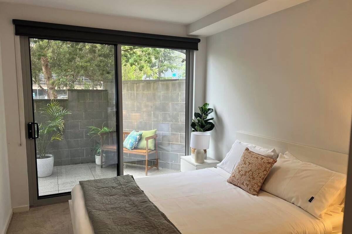 Ein Schlafzimmer mit einem Bett, einer Glasschiebetür, die zu einem Außenbereich mit einer Bank und Pflanzen führt.