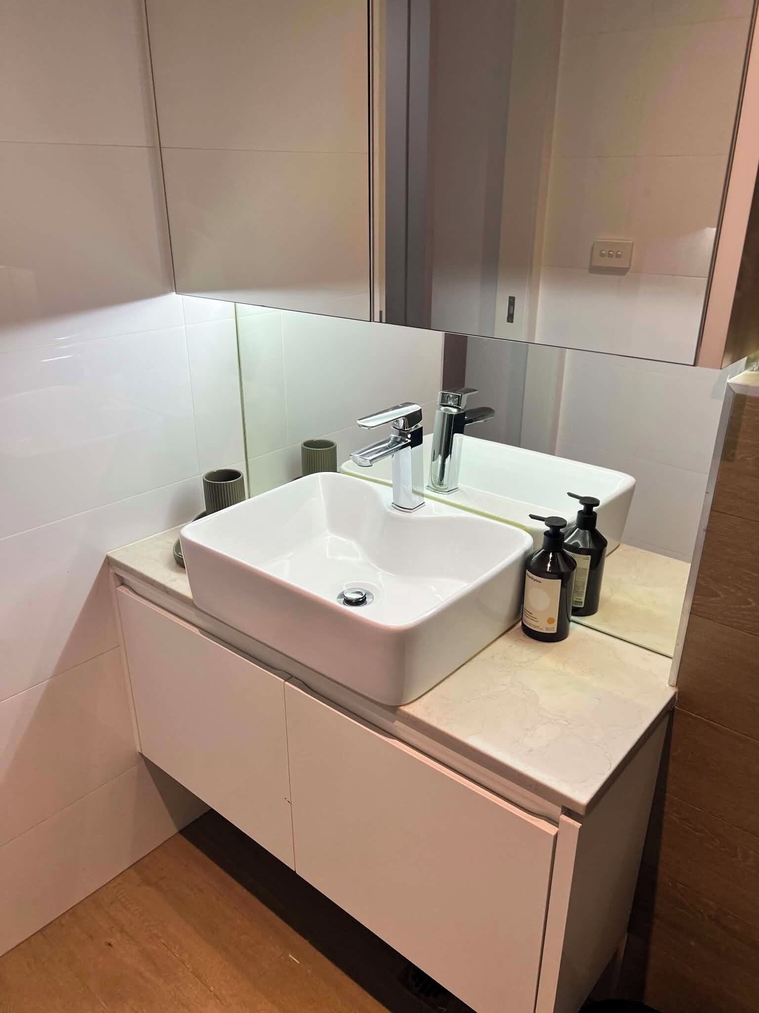 A modern bathroom with a white sink, a mirror, and two bottles of shampoo.