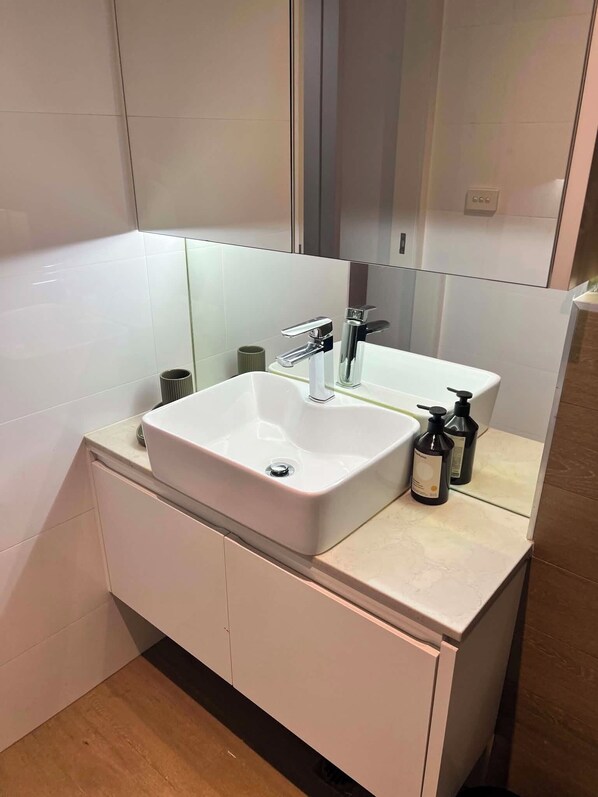 A modern bathroom with a white sink, a mirror, and two bottles of shampoo. - Centrepoint Units Heidelberg (Heidelberg)