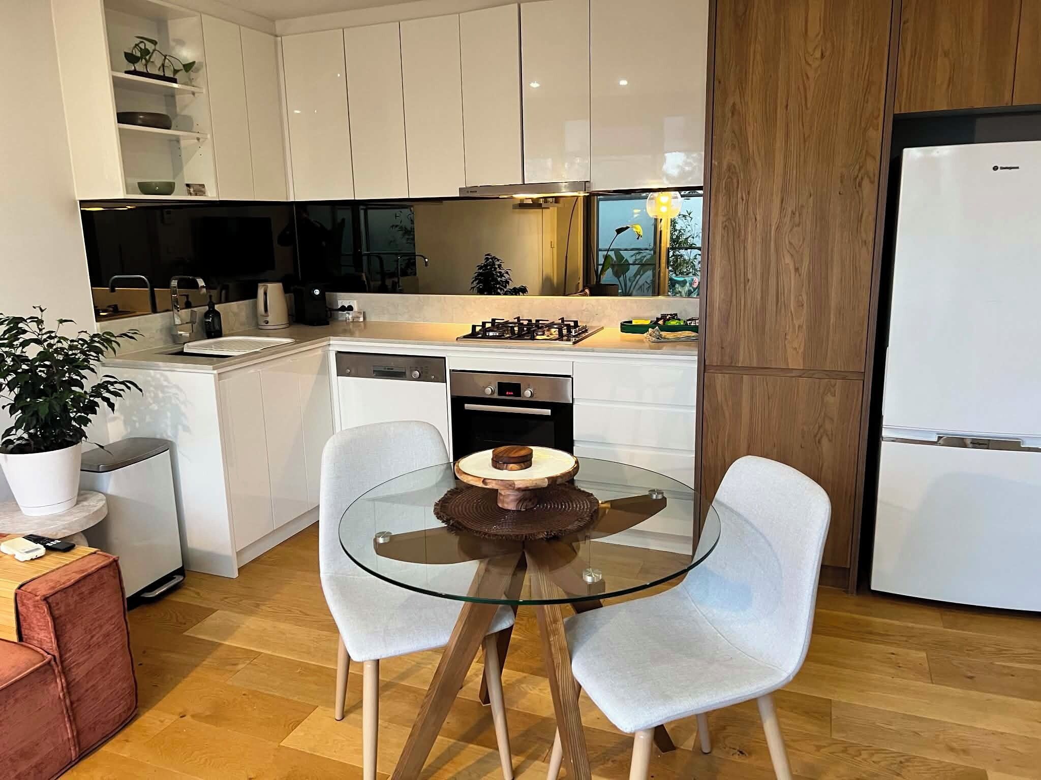 Una cucina moderna con mobili bianchi, un tavolo da pranzo in vetro e un forno integrato.