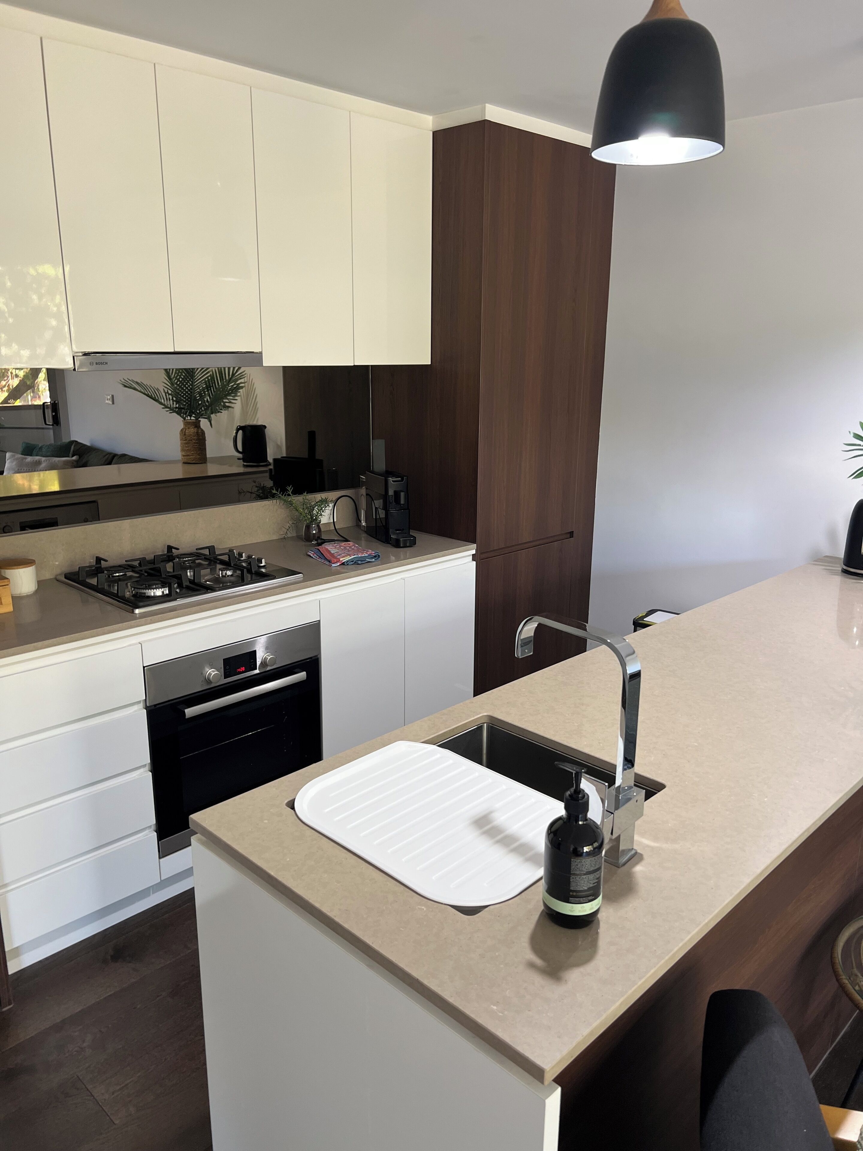 A modern kitchen with white cabinets, a built-in oven, a gas stove, a sink with a faucet, and a pendant light.