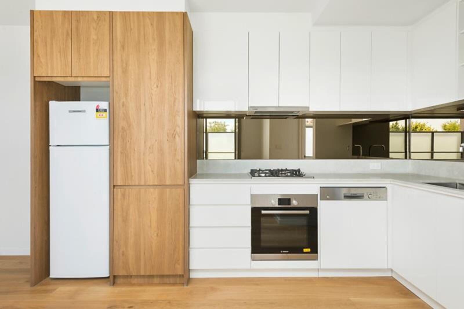 A modern kitchen with white cabinetry, a wooden accent wall, a built-in oven, and a dishwasher.