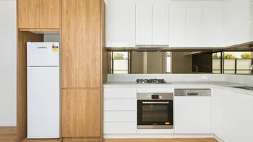 A modern kitchen with white cabinetry, a wooden accent wall, a built-in oven, and a dishwasher.