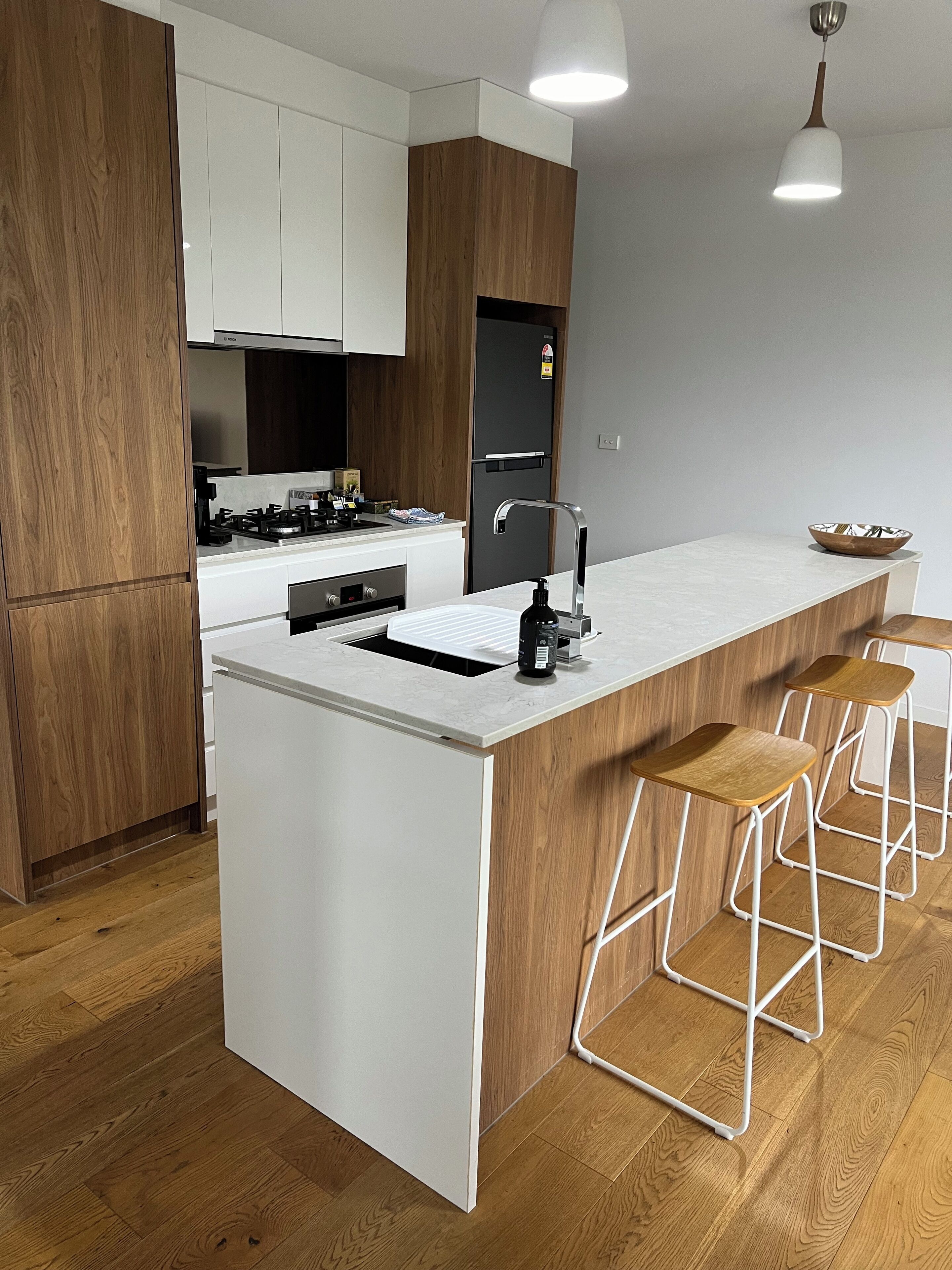 A modern kitchen with white cabinetry, a central island with stools, a stainless steel sink, and a black refrigerator.
