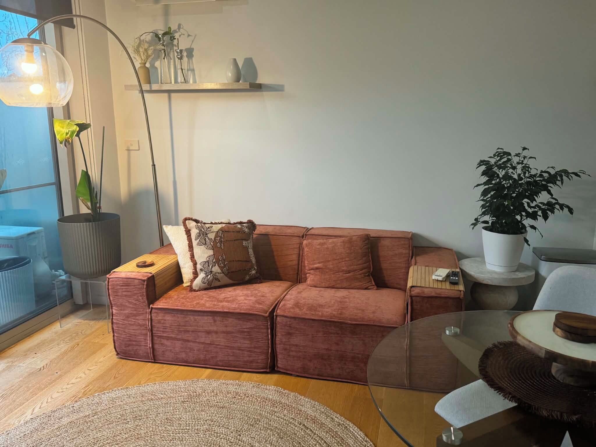 Een moderne woonkamer met een rode bank, een glazen salontafel, een potplant en een vloerlamp.