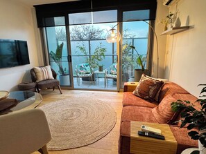 A living room with a sofa, a coffee table, a TV, and a view of a balcony with plants. - Centrepoint Units Heidelberg (Heidelberg)